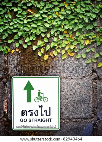Direction sign on green leaf wall