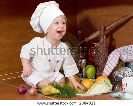 laughing little boy in the cook costume at the kitchen with vegetables