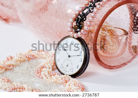 luxury pearl necklaces in the rose crystal vase and antique watch. Focal point is on the watch
