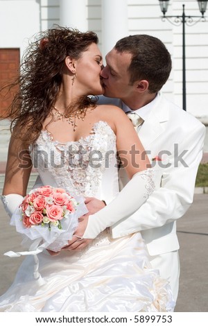 just married - kiss of young couple in wedding wear with bouquet of roses