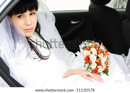young bride in wedding wear with bouquet of roses sitting in the car