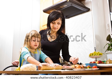 Mother teaching her little daughter how to cook pizza