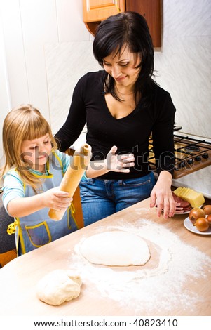 Mother teaching her little daughter how to cook pizza