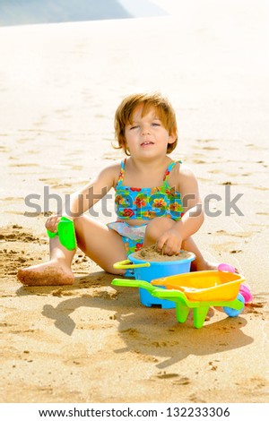 Smiling toddler girl playing with her toys on the beach