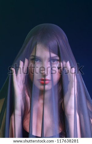 beautiful woman covered by transparent fabric on dark background