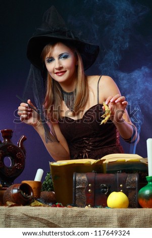 Sexy witch on a dark background making potion looking to the smoke