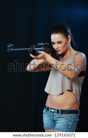 Beautiful sexy woman holding weapon going to shoot over dark background