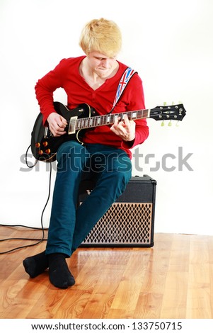 Young man playing guitar sitting over light background
