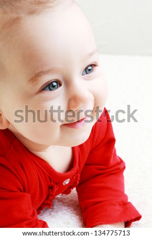 Close-up of sweet little baby laying on the white blanket in red shirt looking serious