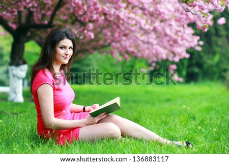 beautiful plus size woman sitting on a grass with book in heer hands under blooming japan cherry trees
