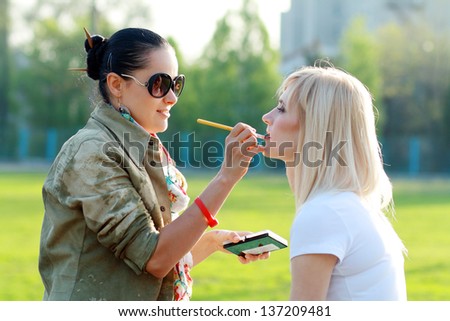 Make-up artist outdoor applying lip liner on model\'s lips, close-up, selective focus on artist