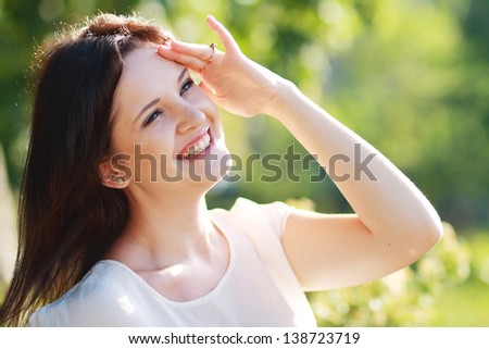 Happy woman looking far away holding hand to brow over green background. Soft summer colors