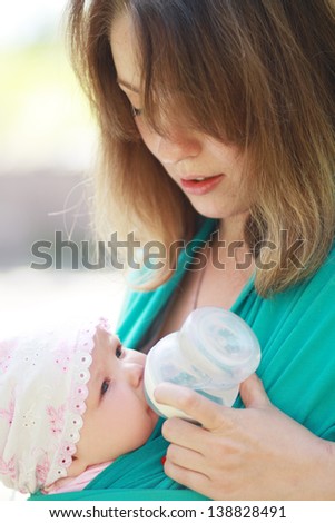 young caring mother gives daughter drink water bottles background summer green park. close up