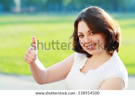 A beautiful young woman giving you a thumb up and smiling in a field with copyspace