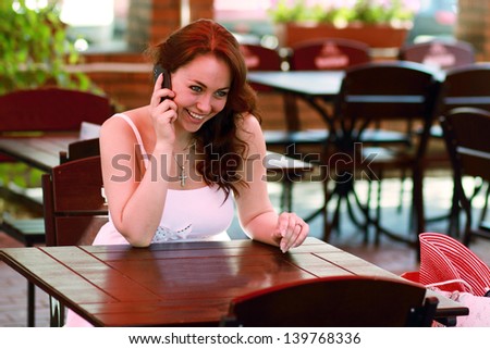 Portrait of young business woman sitting relaxed at outdoor cafe dand chatting using her cell phone