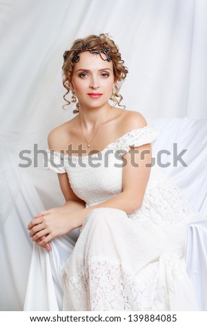 Beautiful woman with romantic bride hairstyle wearing in white wedding dress posing in interior apartment