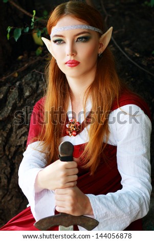 Elf warrior girl on the rock in red cloak posing outdoor