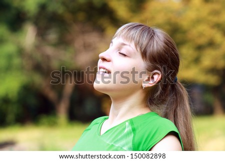Portrait of a pretty young female with closed eyes smiling and breathing fresh air at morning in a park - Outdoor