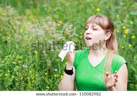 Young woman sneezing in a flowers meadow. Concept: seasonal allergy
