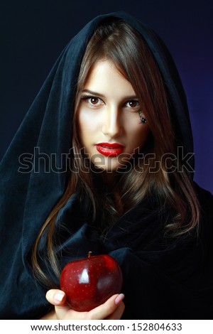 Halloween. Fashion portrait of witch or night vampire woman offering poisoned apple. Bright red lips