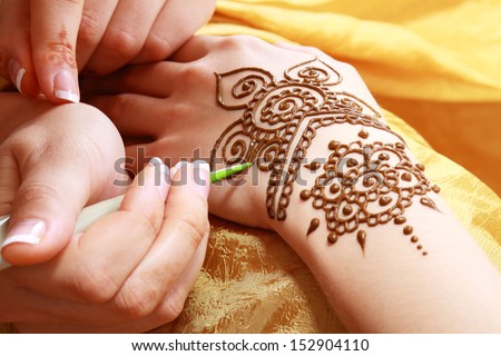 Image detail of henna being applied to hand over golden fabric