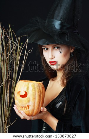 The serious brunette witch with a broom and pumpkin over black background in studio