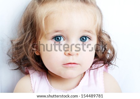 A young little baby girl is looking at the camera with bright blue eyes. Use it for a child or parenthood concept.