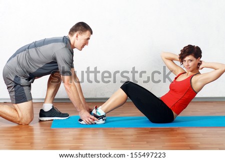 Portrait of a man helping a gorgeous woman to work out in gym
