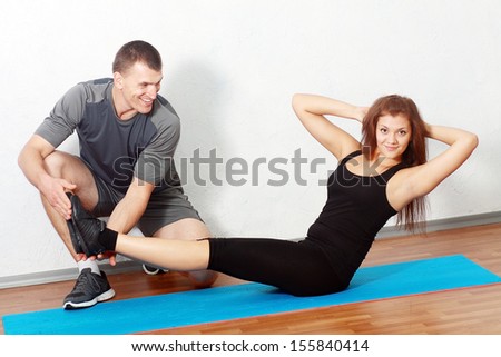 Portrait of a man couch helping a gorgeous woman to work out in gym