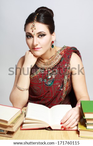 Beautiful indian woman in traditional national clothes with lot of books sitting at the table and studing