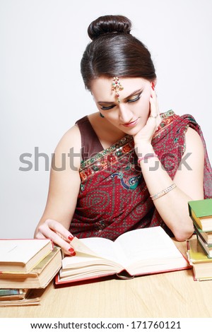 Beautiful indian woman in traditional national clothes with lot of books sitting at the table and studying
