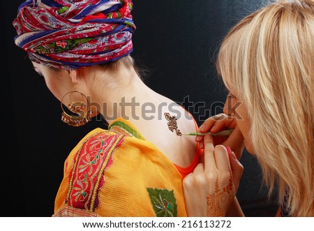 artist draw, picture of process of drawing henna applying on the back of a young girl of Arabic inscriptions, with a focus on the tattoo