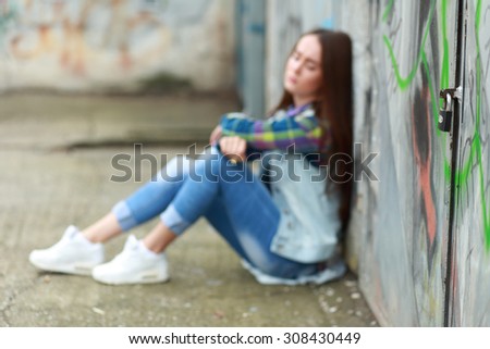 Beautiful young sad girl sitting on asphalt. Girl is out of focus, focus is on the pad lock, no way out concept
