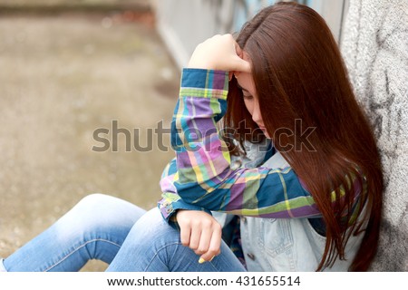 sad lonely teenage girl sitting in urban environment. thinking of teenage problems