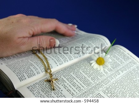 Hand touching pages of open bible, with gold crucifix and flower