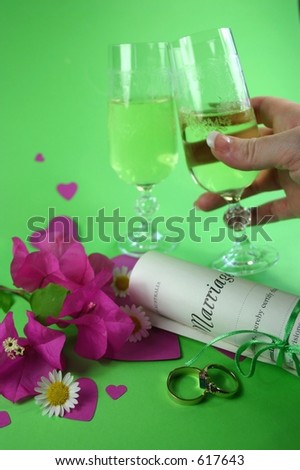 Hand holding champagne glass, with wedding rings, marriage certificate and amongst hearts and flowers