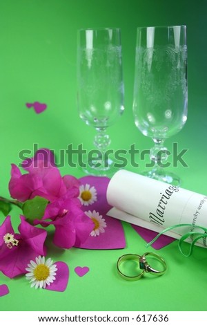 Wedding rings, marriage certificate and champagne glasses amongst hearts and flowers