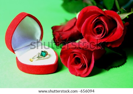 Emerald ring in heart shaped box with red roses on green background