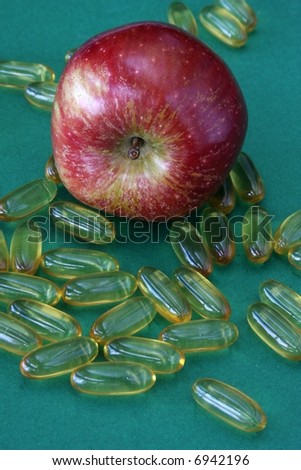 close up of fresh red apple with vitamin pills against green background