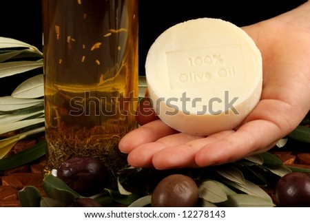 natural olive oil soap olives branch and oil against wooden mat - with hand holding soap
