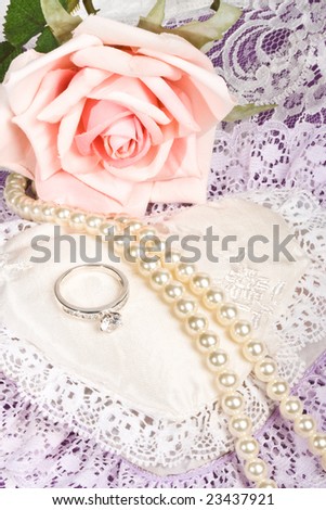 engagement ring, pearl necklace on satin and lace heart pillow with pink silk rose in background