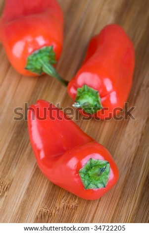 three red peppers / capsicum on wooden cutting board