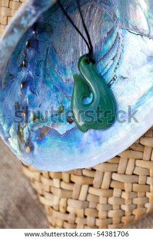 close up of carved maori nephrite jade / greenstone pendant on paua shell with kite bag in background