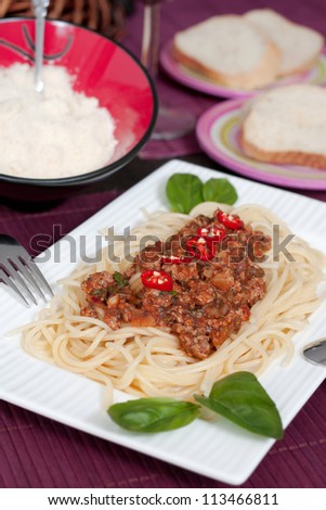 A dish with fresh spaghetti bolognese . ont he table are bread and parmesancheese
