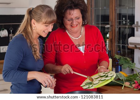 A younger and a older women are cooking in a kitchen and have fun together