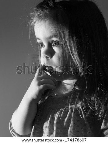 A cute young girl is looking television.She is looking very interested in.Oicture is black and white.