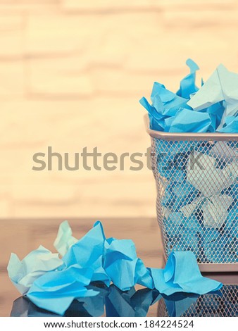 A lot of wrinkled paper laying in and around a wastepaper basket.picture is toned.