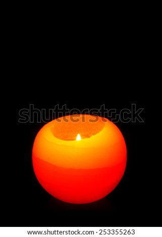 Sphere candle in orange isolated on black. Bright Orange colored candle with a little flame inside.