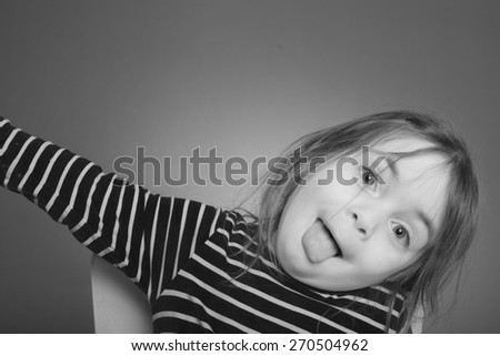 Black and white portrait of a coung girl with a striped t-shirt in front of a gray background . The girl makes a grimace