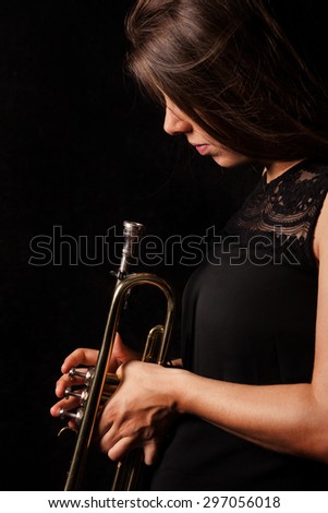 Brownhaired women in front of black backgound is looking on her trumpet
